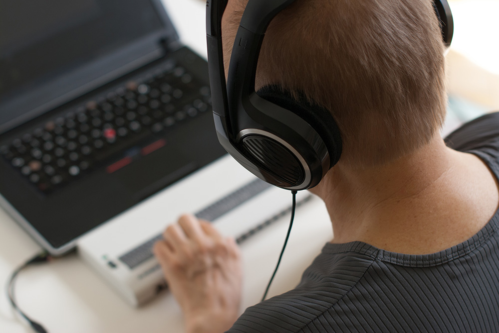 A blind person using a laptop with a screen reader braille device and headphones